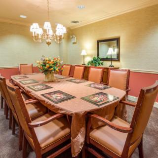 A formal dining room with a large table and chairs, adorned with a chandelier and a central flower arrangement.