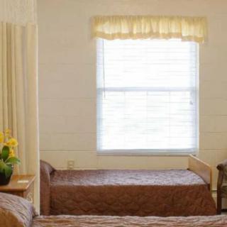 A simple bedroom with two beds, a window with curtains, and a flower arrangement.