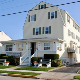 A three-story residential building with green shutters, featuring a lawn and shrubs in the front.