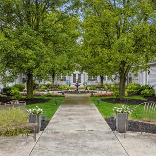 A scenic garden pathway leading towards a white building, surrounded by lush greenery and trees.