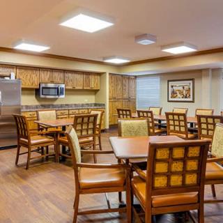 A well-lit dining area with wooden furniture and a kitchen setup.