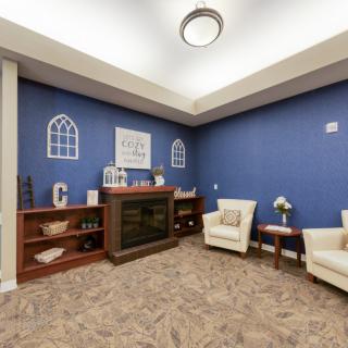 A cozy living room with blue walls, featuring armchairs and a fireplace alongside decorative bookshelves.