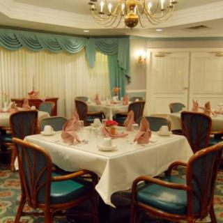 An elegant dining room with neatly arranged tables and chairs, featuring ornate table settings and a chandelier.