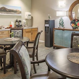 A cozy dining area with neatly arranged tables and chairs, warm lighting, decorative artwork, and a beverage station.