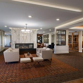 A modern living room interior with a central fireplace surrounded by stylish furniture and a decorative ceiling.
