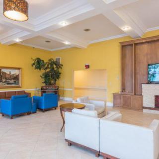 A modern lobby with bright yellow walls, featuring comfortable seating with white couches and blue chairs, complemented by indoor plants and a television.