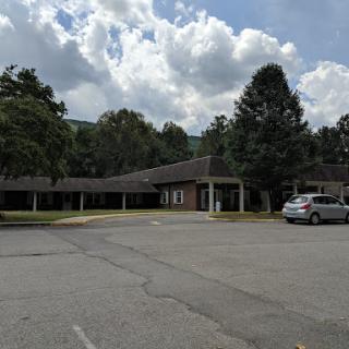 A view of a single-story building surrounded by trees under a partly cloudy sky.
