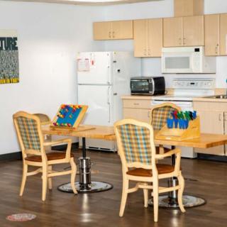 A kitchen and dining area with light wood cabinetry, featuring a refrigerator, microwave, and seating for four at two tables.