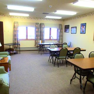 A cozy community room set up with tables and chairs, featuring large windows that bring in natural light.