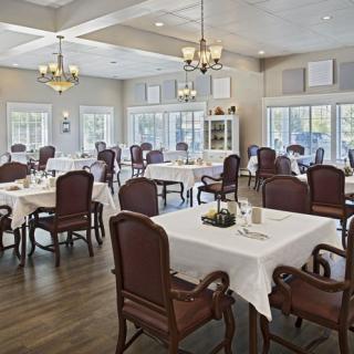 An elegant dining room with neatly arranged tables and chairs, illuminated by chandeliers and natural light.
