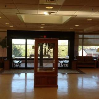 A lobby area with glass doors and a central display case, flanked by seating areas.