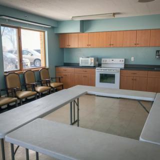 A multi-purpose room featuring a kitchen area with appliances and a U-shaped table setup with chairs.