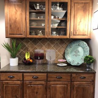 A kitchen setup with wooden cabinets, glass door display, and countertop decorations including a plant, fruit bowl, and decorative plate.