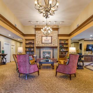 A cozy living room with elegant chandeliers and a fireplace, surrounded by comfortable seating and bookshelves.