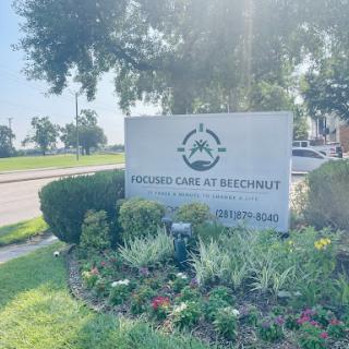 A welcoming sign for a healthcare facility, surrounded by greenery and flowers.