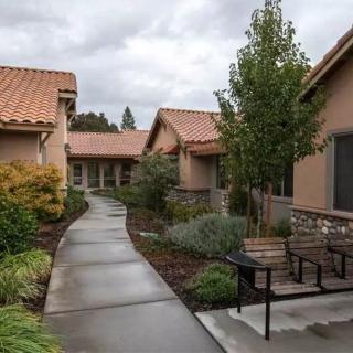 A pathway leads through a residential area with neatly landscaped gardens and houses under an overcast sky.