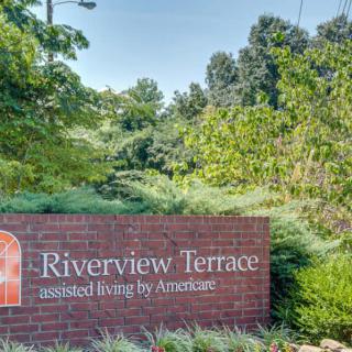 A brick sign for Riverview Terrace assisted living surrounded by lush greenery.