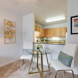 A cozy dining area with a glass table and two white chairs, adjacent to a modern kitchen.