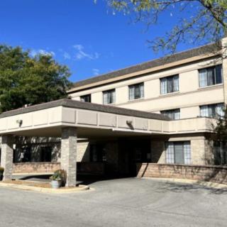 A three-story hotel building with a covered entrance, surrounded by trees and a clear blue sky.