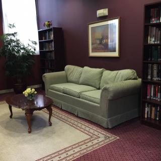 A cozy living room with a green sofa, a coffee table with flowers, bookshelves, and a decorative rug.