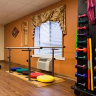 A therapy room featuring parallel bars, colorful cushions, and a rack of weights for rehabilitation exercises.