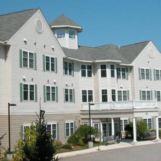 A three-story residential building with a large porch and multiple windows surrounded by small trees.