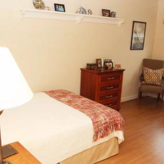 A cozy bedroom with a bed, dresser, and chair, featuring warm decor.