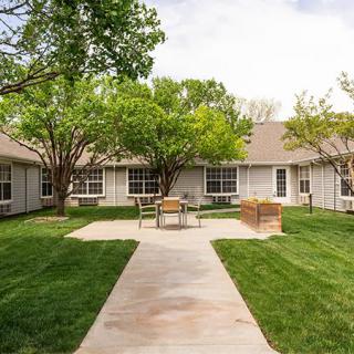 A peaceful courtyard with green grass, trees, and outdoor seating surrounded by a building.