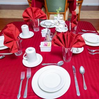 A neatly arranged dining table with a red tablecloth, featuring plates, cutlery, and folded napkins.
