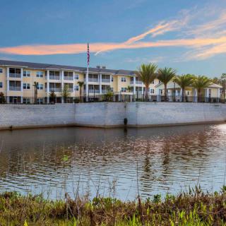 A modern building with palm trees reflected in a nearby body of water under a colorful sky.