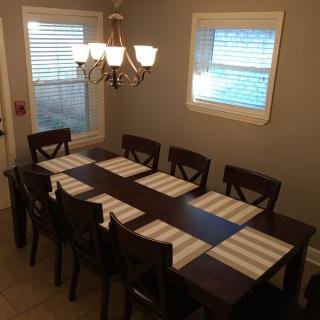 A dining room with a large table set for eight, adorned with striped placemats and illuminated by a chandelier.