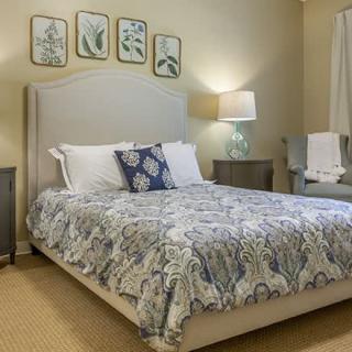 A cozy and elegantly decorated bedroom with a patterned bedspread, framed artwork, and a bedside lamp.
