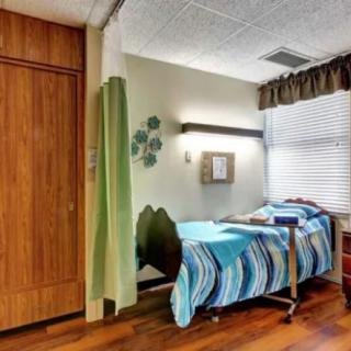 A hospital room with a single bed, privacy curtain, and wooden flooring.