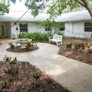 A peaceful courtyard with a curved pathway, surrounded by lush greenery and featuring a bench for outdoor seating.