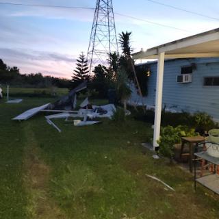 Damage near a house caused by a fallen structure, captured during the evening.