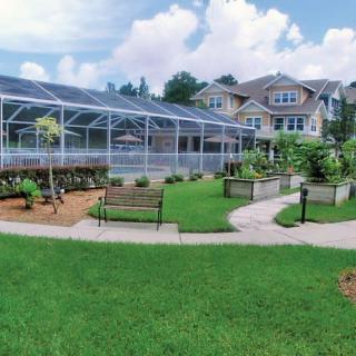 A scenic backyard with a greenhouse, well-maintained garden, and comfortable benches leading to a large house.