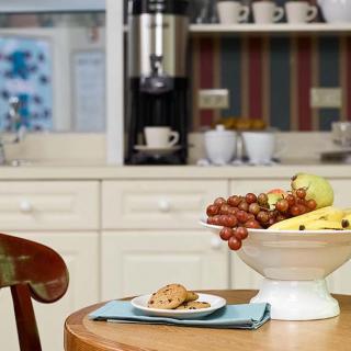 A cozy kitchen setting with a fruit bowl and cookies on a table, accompanied by a coffee maker in the background.