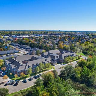 Aerial view of a suburban neighborhood with buildings, lush greenery, and a clear blue sky.