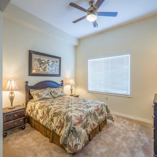 A cozy bedroom with a bed, side tables, lamps, and a ceiling fan.