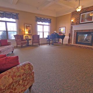 A cozy living room with a fireplace and a grand piano, complemented by comfortable seating and large windows.