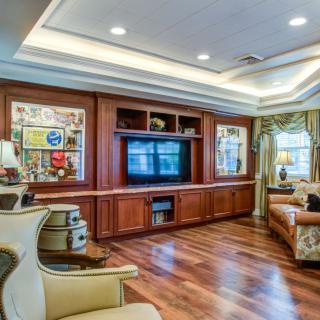 A spacious living room featuring hardwood flooring, a large television set into a wooden entertainment center, comfortable sofas, and decorative wall art under ceiling lights.