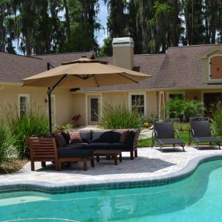 A serene backyard with a swimming pool, patio furniture, and an umbrella for shade.