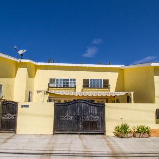 A bright yellow residential house with a gated entrance under a clear blue sky.
