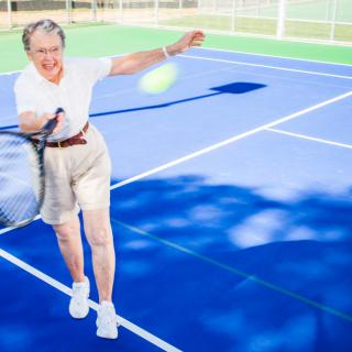A senior woman enjoying a game of tennis on an outdoor court.