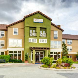 Exterior view of a hotel building with a landscaped entrance under a cloudy sky.