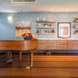 A stylish living room featuring a grand piano, wooden floors, and decorative shelves with artwork.