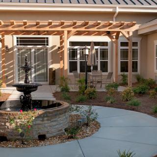 A serene courtyard featuring a central fountain, surrounded by landscaped garden and a patio area.