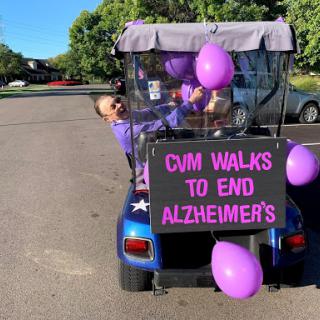 A spirited participant promotes Alzheimer's awareness while riding in a decorated golf cart at a community event.