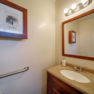 A small bathroom with a sink, mirror, wall art, and lighting above the mirror.