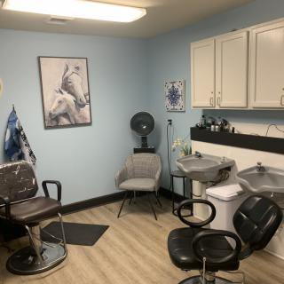 A tidy barber shop interior featuring chairs, a hair-washing sink, and a wall poster.